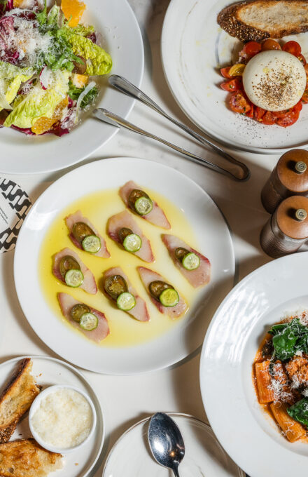 Two beds in a hotel room with white linens, wood paneling, a mirrored headboard, hanging pendant lights, and a plush carpet. There's a glass-walled bathroom visible in the background.