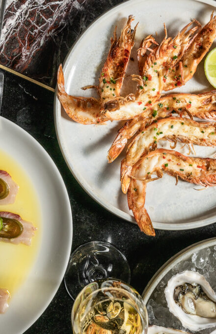 A cozy hotel bedroom featuring a large bed with white linens, a brown headboard, a side table with a lamp, and elegant wall art above the bed.