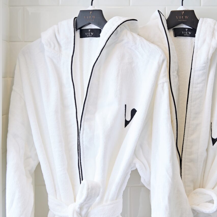 A cozy hotel room with a large bed, plush pillows, a desk with a chair, a window with curtains, and decorative artwork on the wall.