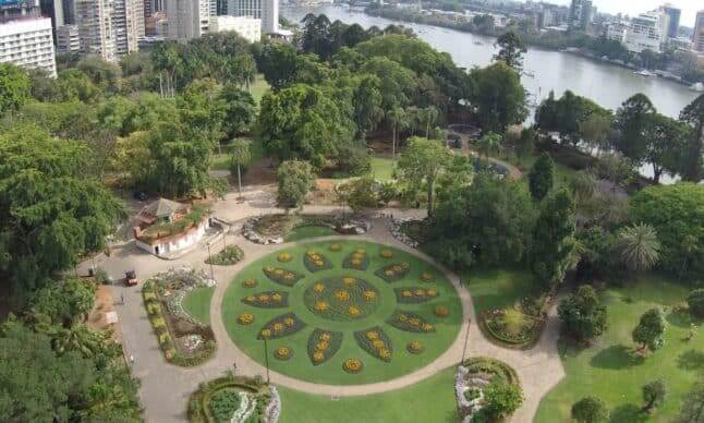 Aerial view of lush hotel gardens with vibrant flower beds, riverfront, and cityscape, offering serene relaxation and nature walks.