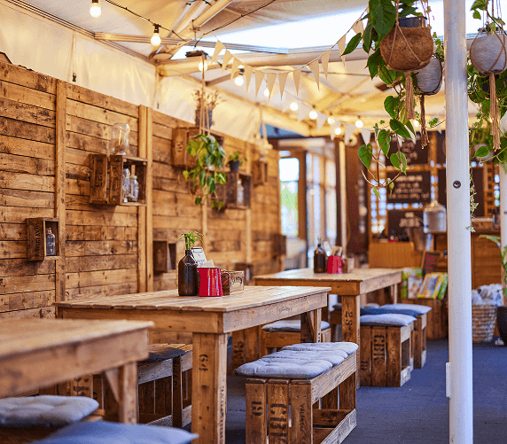 Stylish rustic hotel terrace with wooden tables, cosy cushions, pendant lights, and lush greenery enhancing a warm ambience.