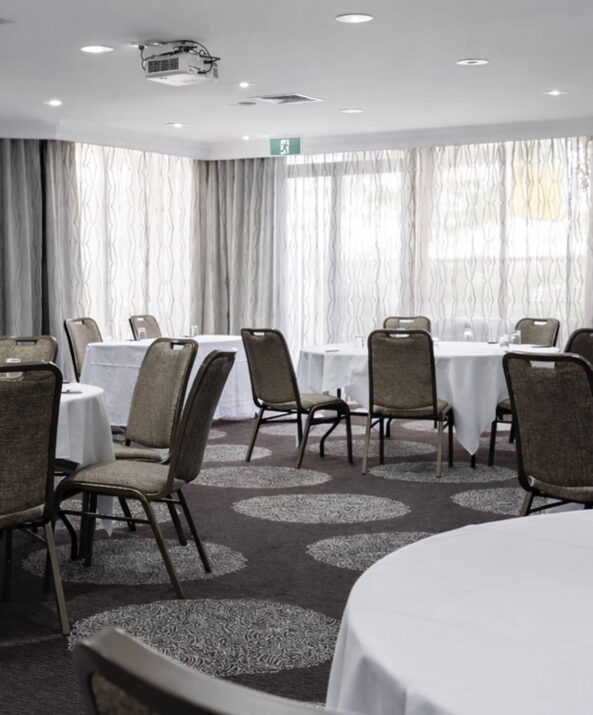 Spacious hotel conference room with round tables, elegant lighting, and presentation screen for events and meetings.