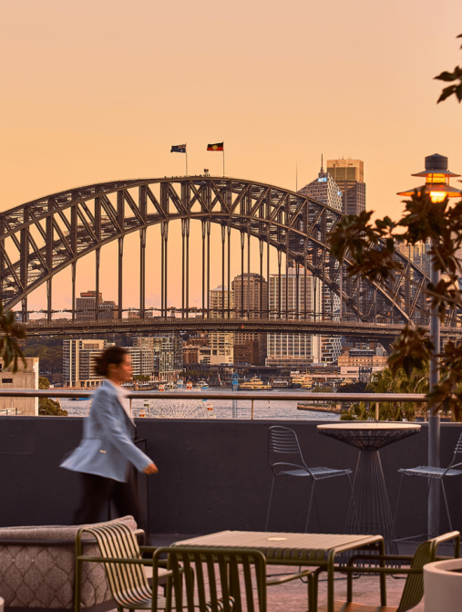 Rooftop lounge with stunning sunset view of Sydney Harbour Bridge, ideal for relaxation and enjoying exquisite hotel amenities.