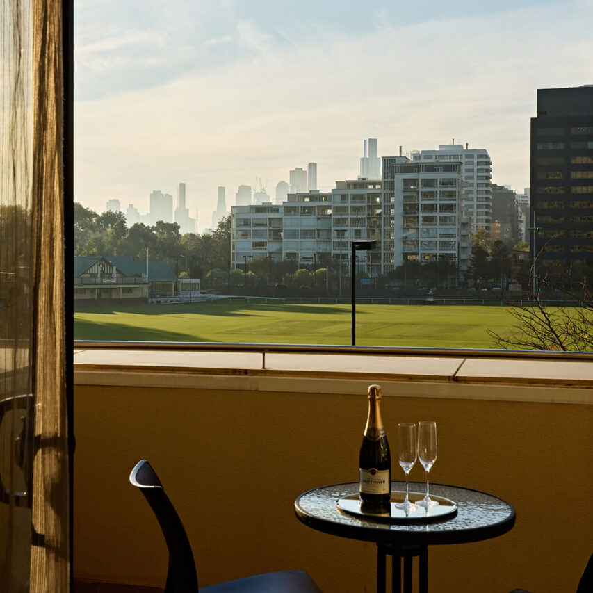 Balcony with city view, bistro table, champagne, and melbourne skyline in hotel suite.