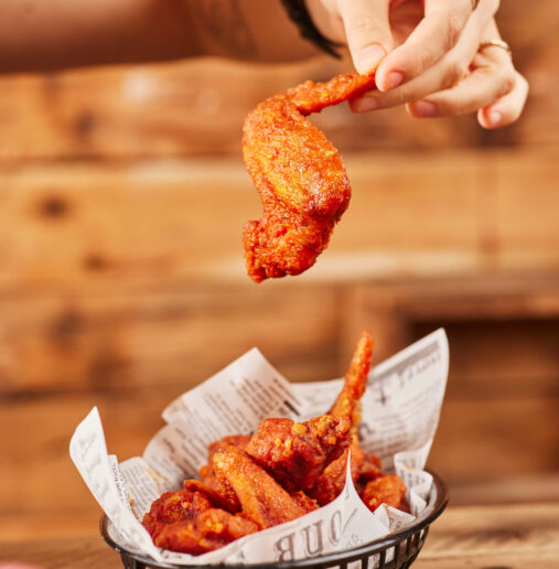 A modern outdoor garden area with a wooden deck, surrounded by lush greenery, and featuring comfortable seating arrangements including chairs, tables, and a large parasol for shade.