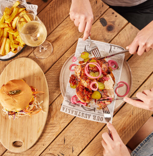 A modern hotel building with large windows and balconies, surrounded by lush green trees and a well-maintained lawn under a clear blue sky.