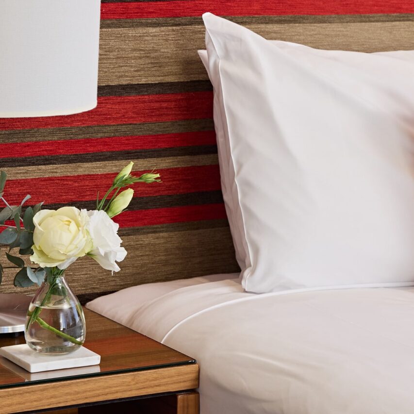 A modern hotel exterior with glass windows, palm trees, and a clear blue sky, showcasing a welcoming urban atmosphere.