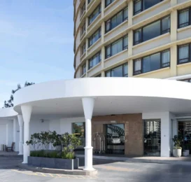 Modern hotel entrance with elegant curved canopy, large windows, and welcoming garden, promising a luxurious stay.