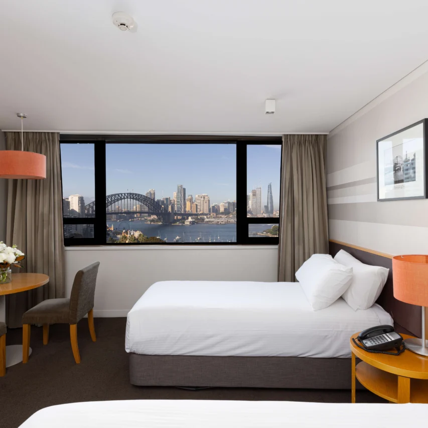 Spacious hotel room with a city skyline view, cosy seating area, modern decor, and a comfortable bed. Ideal for relaxing stays.