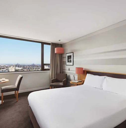 Bright hotel room with a city view, cosy seating area, comfortable double bed, and modern decor inviting relaxation.