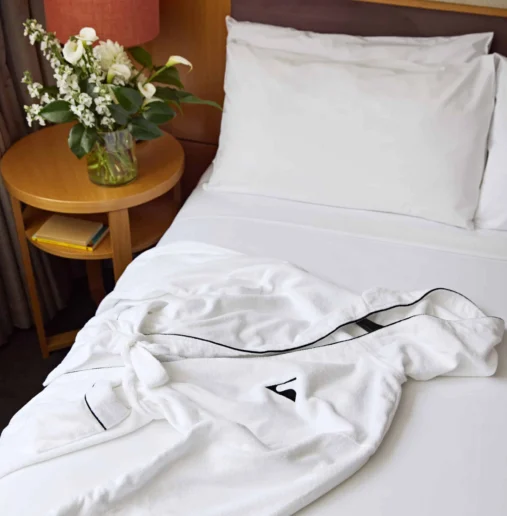 Luxurious hotel bed with crisp white linen, plush robe, and elegant flowers on a bedside table for a relaxing stay.