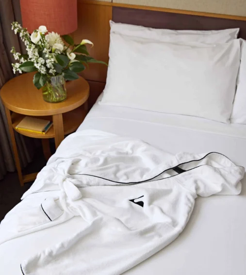Luxurious hotel bed with crisp white linen, plush robe, and elegant flowers on a bedside table for a relaxing stay.