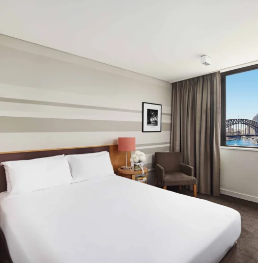 Modern hotel room with plush bed, city view, and Harbour Bridge, ideal for a comfortable stay and scenic experience.