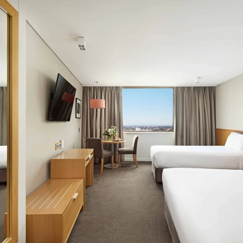 Spacious twin hotel room with city view, flat-screen TV, elegant sitting area, and comfortable beds for relaxing stay.