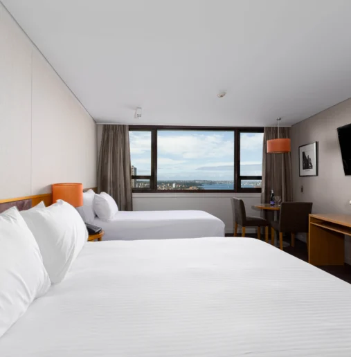 Spacious hotel room with sea view, two cosy beds, flat-screen TV, desk, modern decor, warm lighting, inviting ambience.
