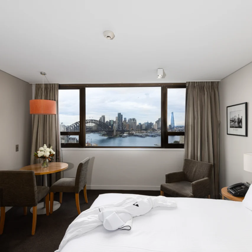 Hotel room with Harbour Bridge view, plush double bed, sitting area, and modern amenities for a relaxing stay.