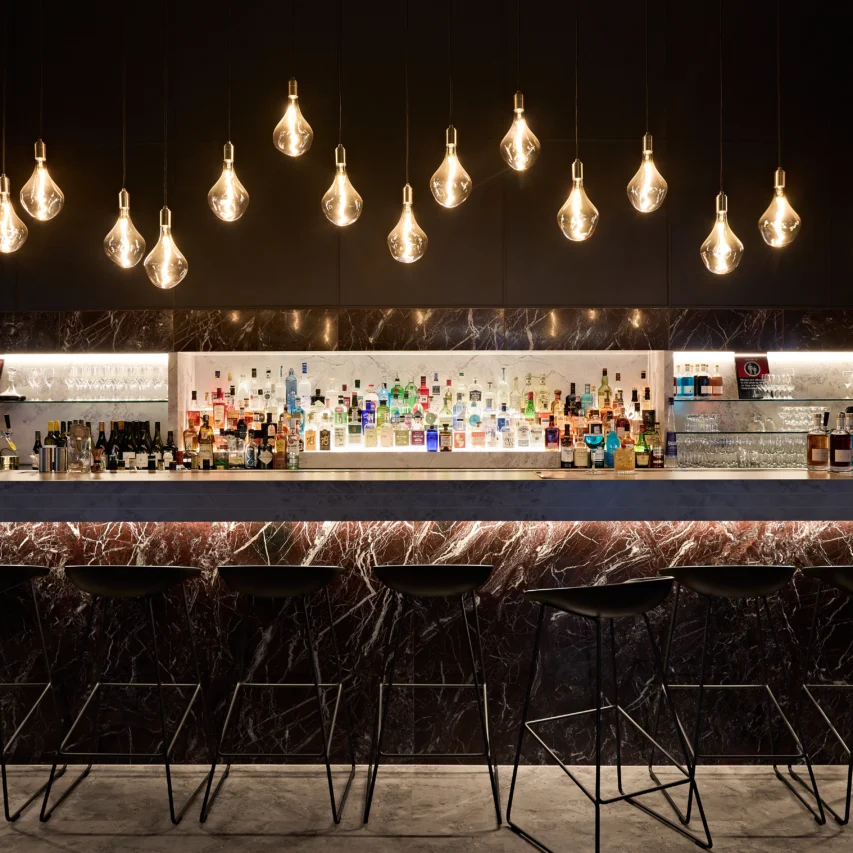 Chic hotel bar with modern lighting and a stocked drinks display, inviting seating, perfect for evening relaxation.
