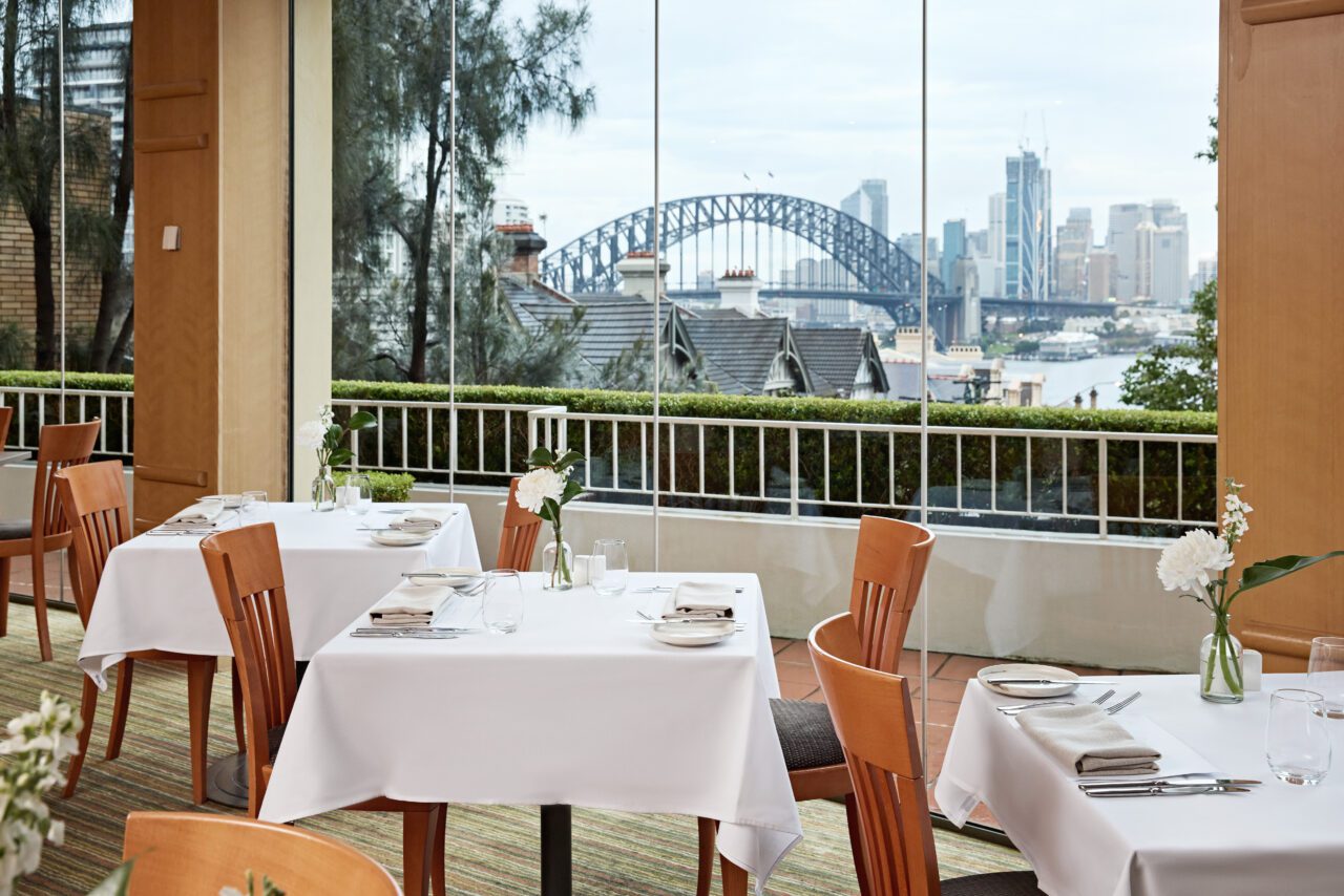 Restaurant tables arranged near a window overlooking the Sydney Harbour Bridge.