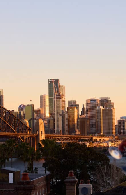 Woman drinking champagne looking out at harbour bridge at sunset