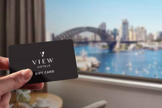 Sydney Harbour view with iconic Opera House and Harbour Bridge. The image features a gift card with "VIEW Hotels" branding, showcasing a cityscape with blue sky and water.