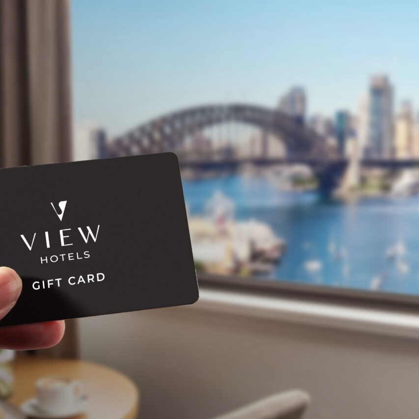 Sydney Harbour view with iconic Opera House and Harbour Bridge. The image features a gift card with "VIEW Hotels" branding, showcasing a cityscape with blue sky and water.