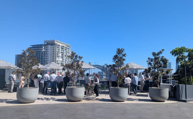 zoomed out shot of group enjoying canapes and drinks on a blue sky day overlooking the Sydney Harbour Bridge