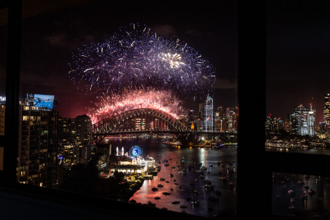 A stunning fireworks display over Sydney Harbour Bridge, illuminating the night sky during New Year's Eve celebration, with vibrant colors reflecting on the water below.