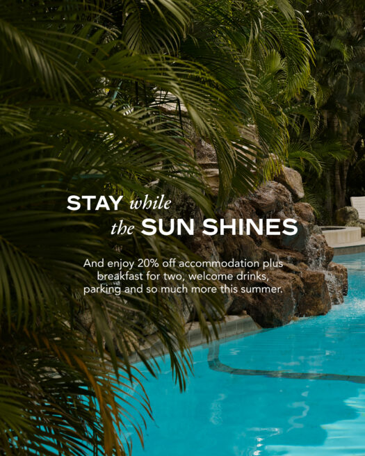 A cityscape of Brisbane, featuring the iconic Story Bridge, skyscrapers, and a clear blue sky reflecting on the Brisbane River.