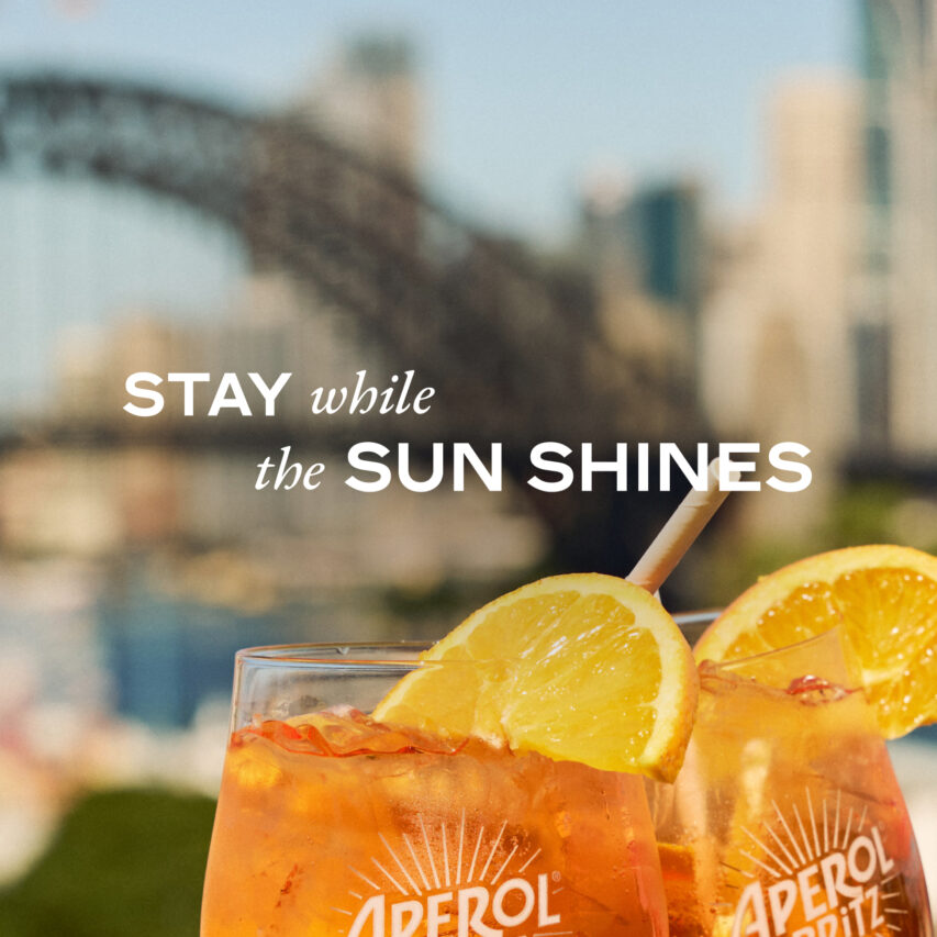 A diverse group of smiling individuals, standing closely for a group photo, in a well-lit interior space with neutral-colored walls and a simple, modern décor.