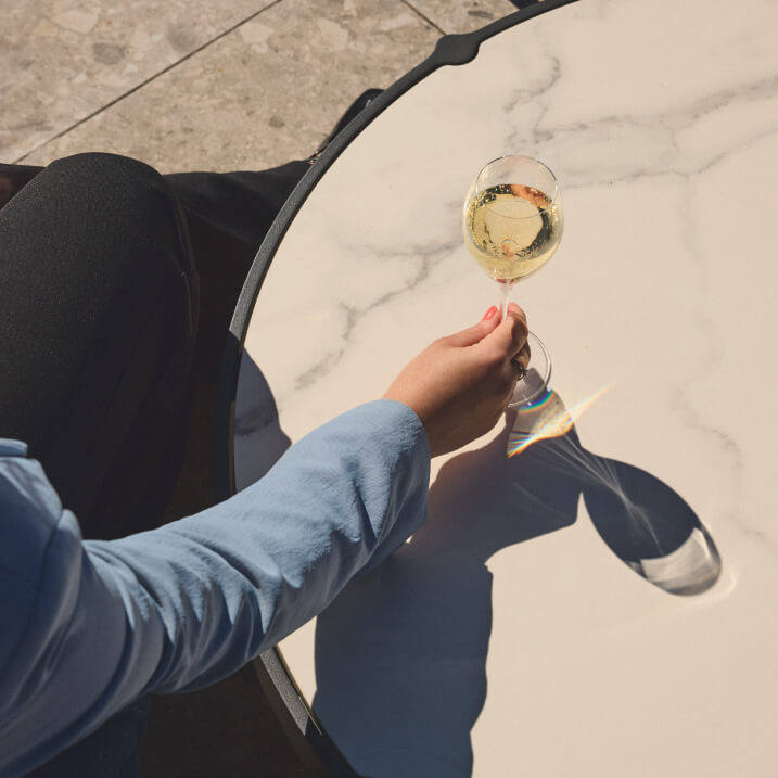 A hotel suite with large windows, featuring a bed, armchair, and side table overlooking a cityscape. The decor is modern and minimalist.