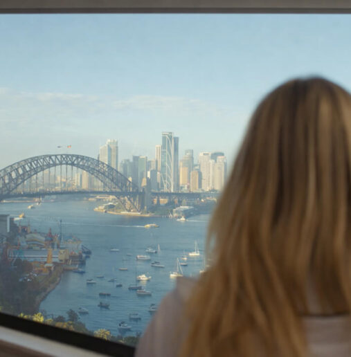 A modern hotel room with a large bed, white linens, green accent pillows, a wall-mounted TV, a desk, and a window with city views.