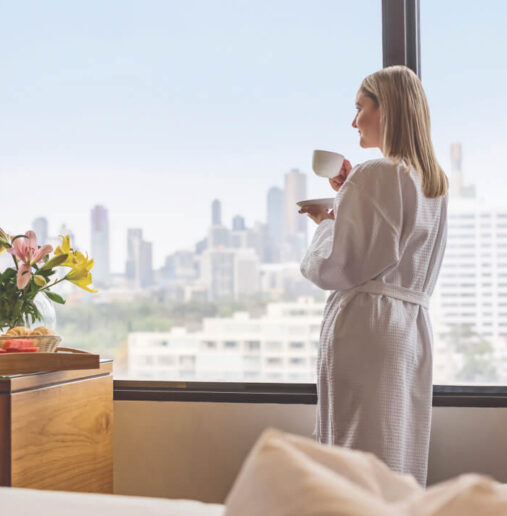 Image of a couple enjoying a romantic dinner outdoors at a restaurant terrace with cityscape and sunset in the background. Richly decorated table setting with candles and flowers.