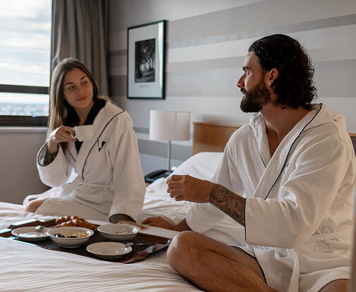 A modern hotel exterior featuring a series of large, reflective glass windows during the daytime, with an entrance partially visible and a clear blue sky in the background.