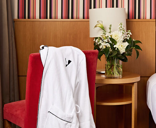 Image showing a modern hotel with sleek glass architecture, surrounded by trees and a vibrant cityscape, under a clear blue sky.