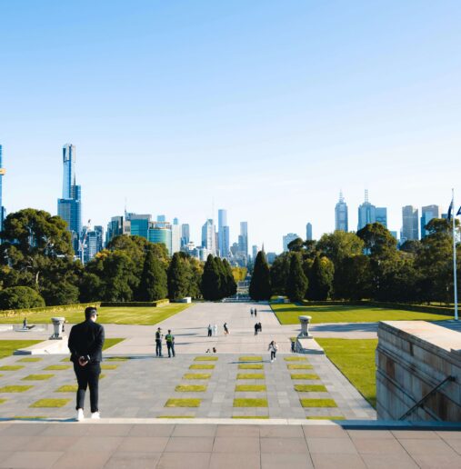 A spacious hotel room with two neatly made beds, wooden furnishings, large windows, and a scenic view of a coastline. Soft lighting creates a warm and inviting atmosphere.