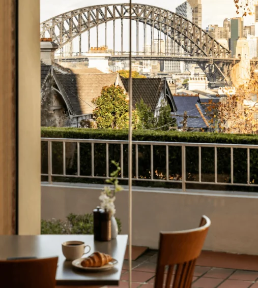 A buffet breakfast spread featuring various pastries, fruits, cereals, and drinks displayed on a marble countertop, with a view of a city skyline through large windows in the background.