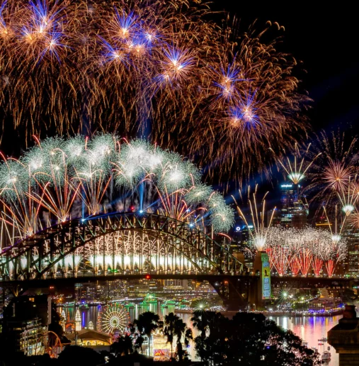 Stunning city view of vibrant fireworks over illuminated harbour bridge and skyline, perfect for New Year celebrations.