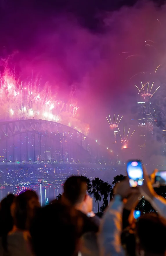 Guests enjoy fireworks over Sydney Harbour Bridge from luxurious rooftop hotel terrace, capturing vibrant cityscape views.